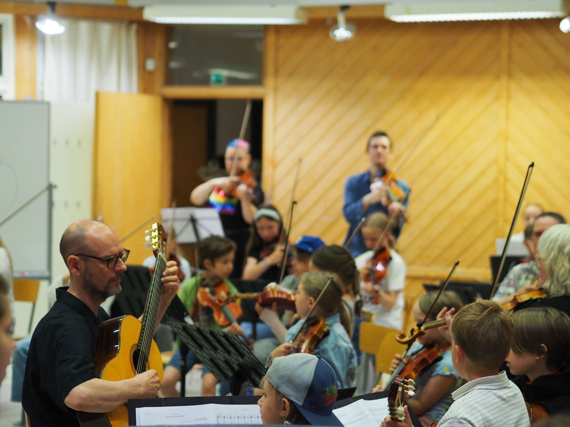 En musiklärare spelar gitarr framför en grupp barn.