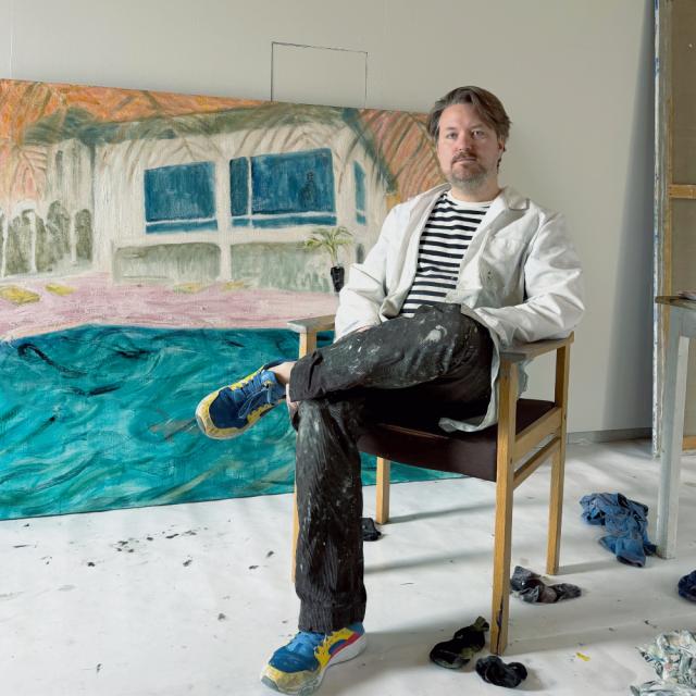 Erik Creutziger sitter på en stol framför en av sina egna tavlor.